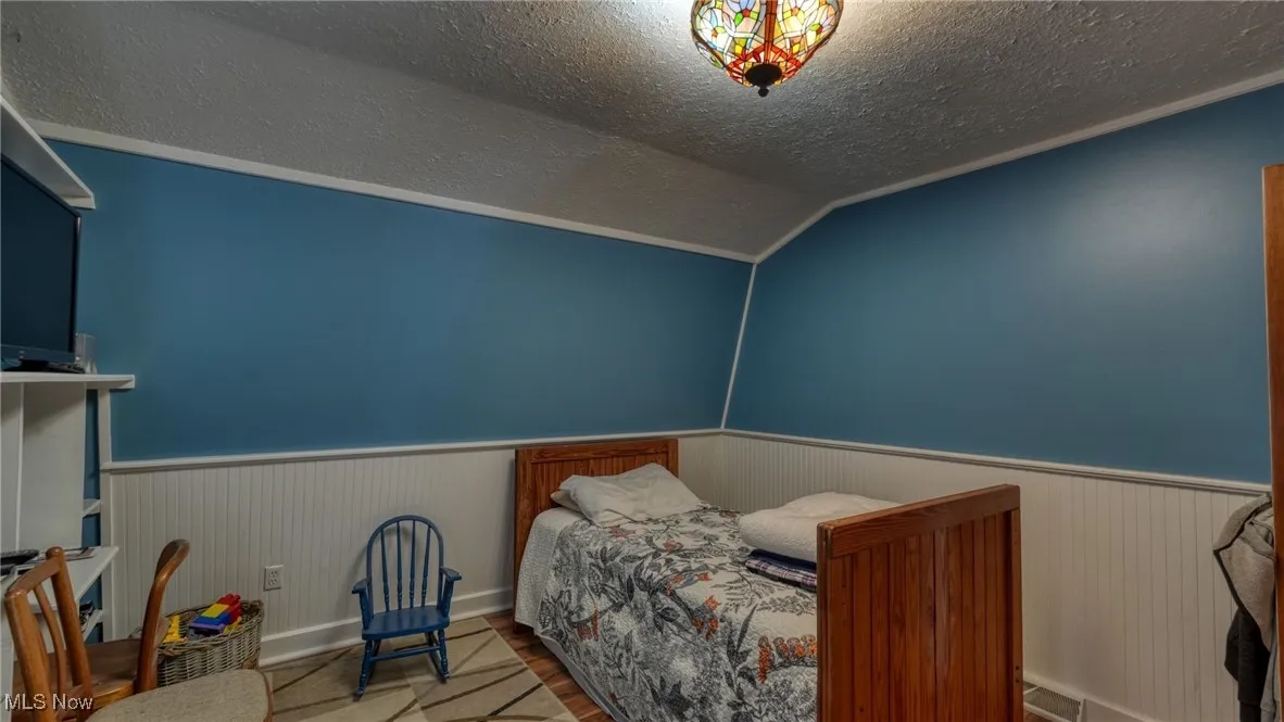 Bedroom featuring lofted ceiling, wood-type flooring, and a textured ceiling