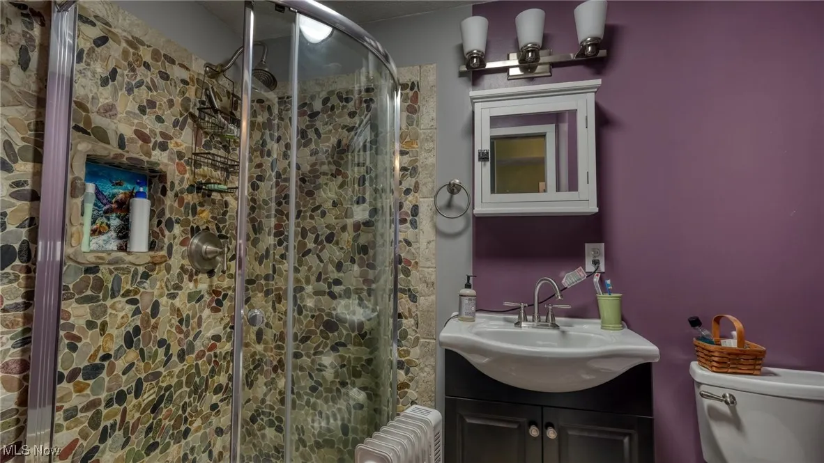 Bathroom featuring vanity, a shower with shower door, radiator, and toilet