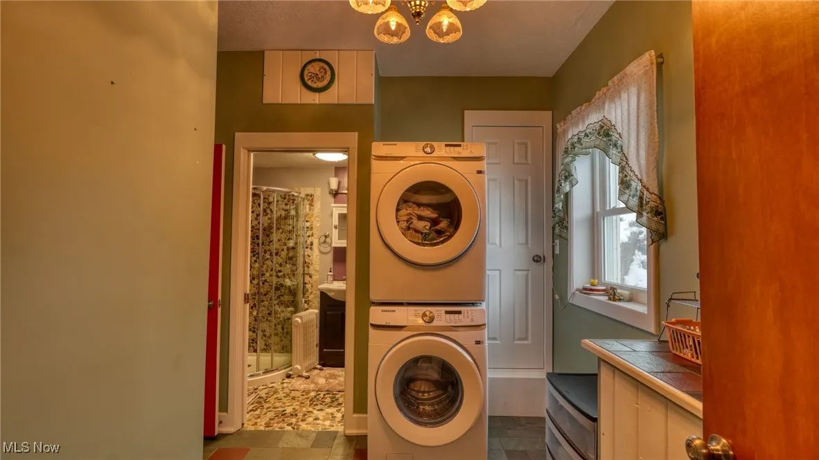 Washroom with an inviting chandelier and stacked washer / dryer