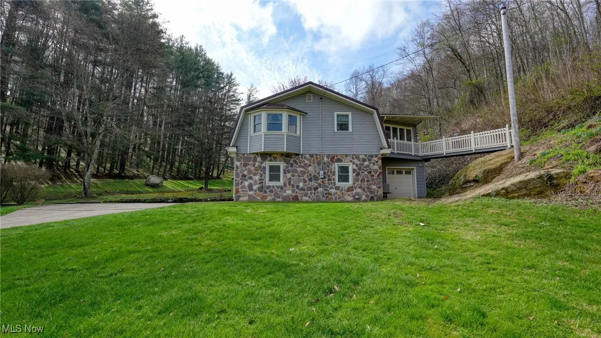 View of front of house with a gambrel roof, an attached garage, a front lawn, and stone siding