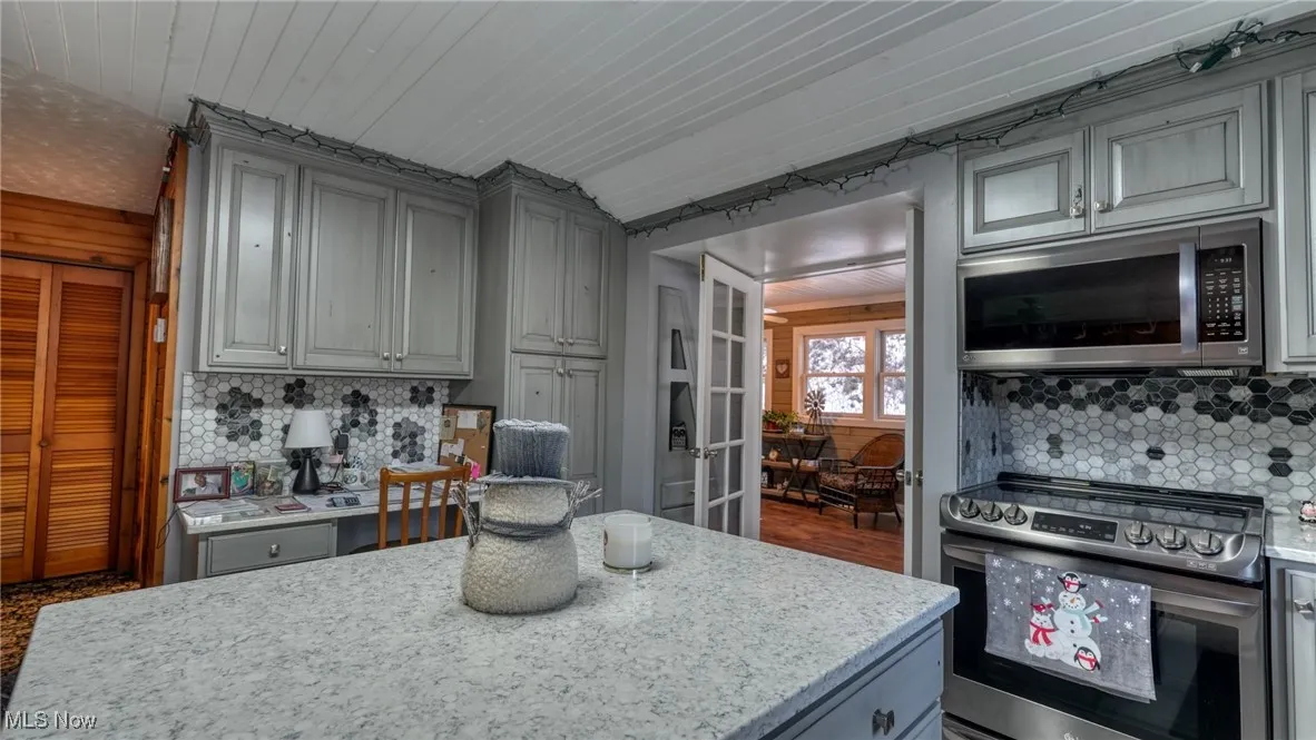 Kitchen featuring appliances with stainless steel finishes, tasteful backsplash, gray cabinetry, a center island, and light stone counters