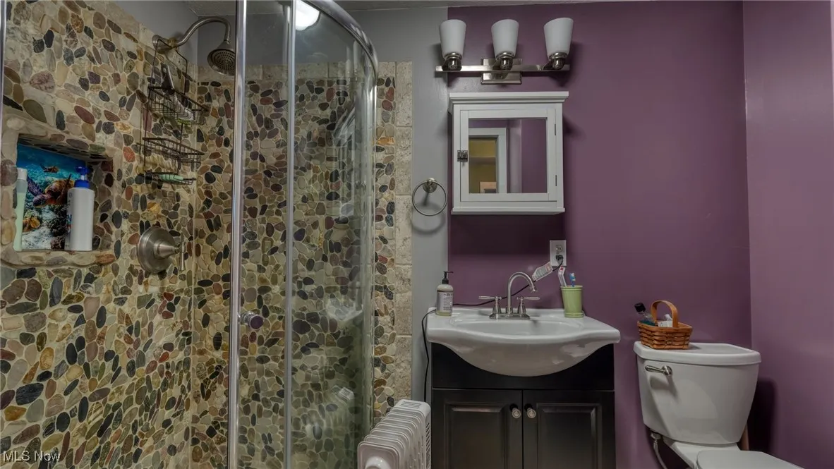 Bathroom featuring vanity, a shower with shower door, radiator, and toilet