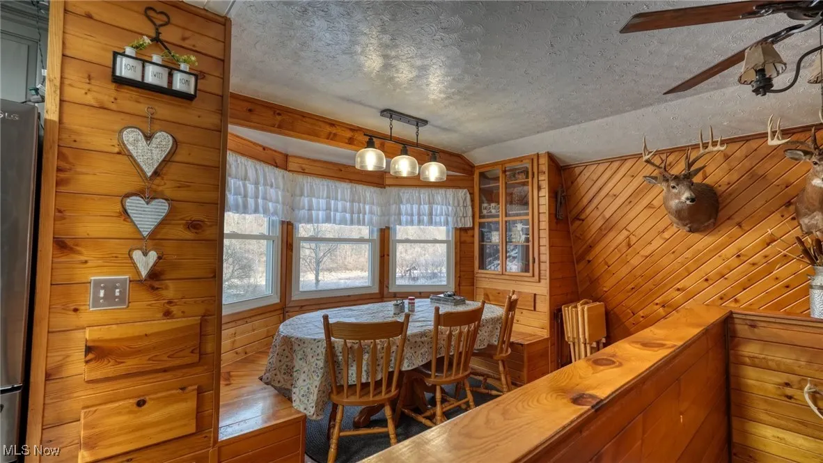 Dining room with lofted ceiling, wood-type flooring, a textured ceiling, wooden walls, and ceiling fan