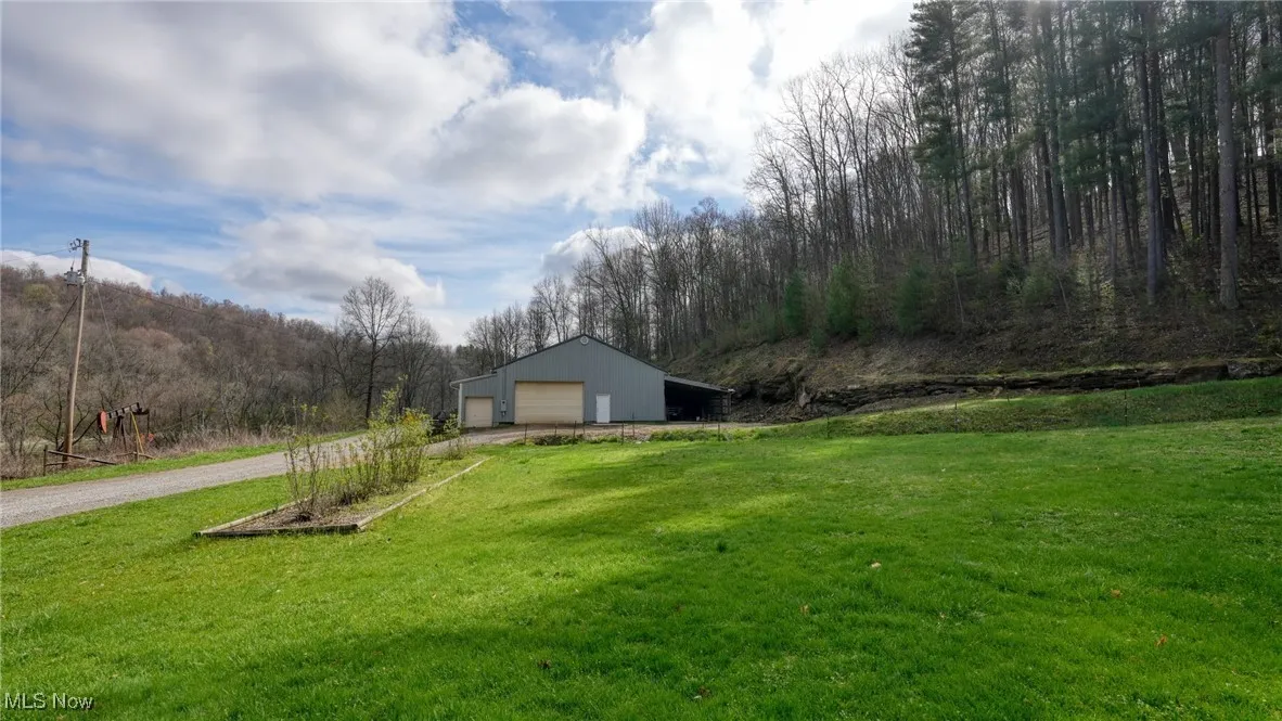View of yard featuring an outbuilding, a pole building, a view of trees, a garage, and driveway