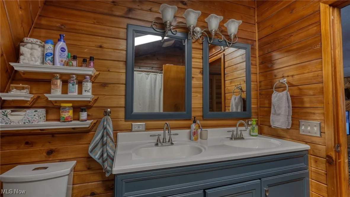 Bathroom featuring vanity, a notable chandelier, toilet, and wood walls