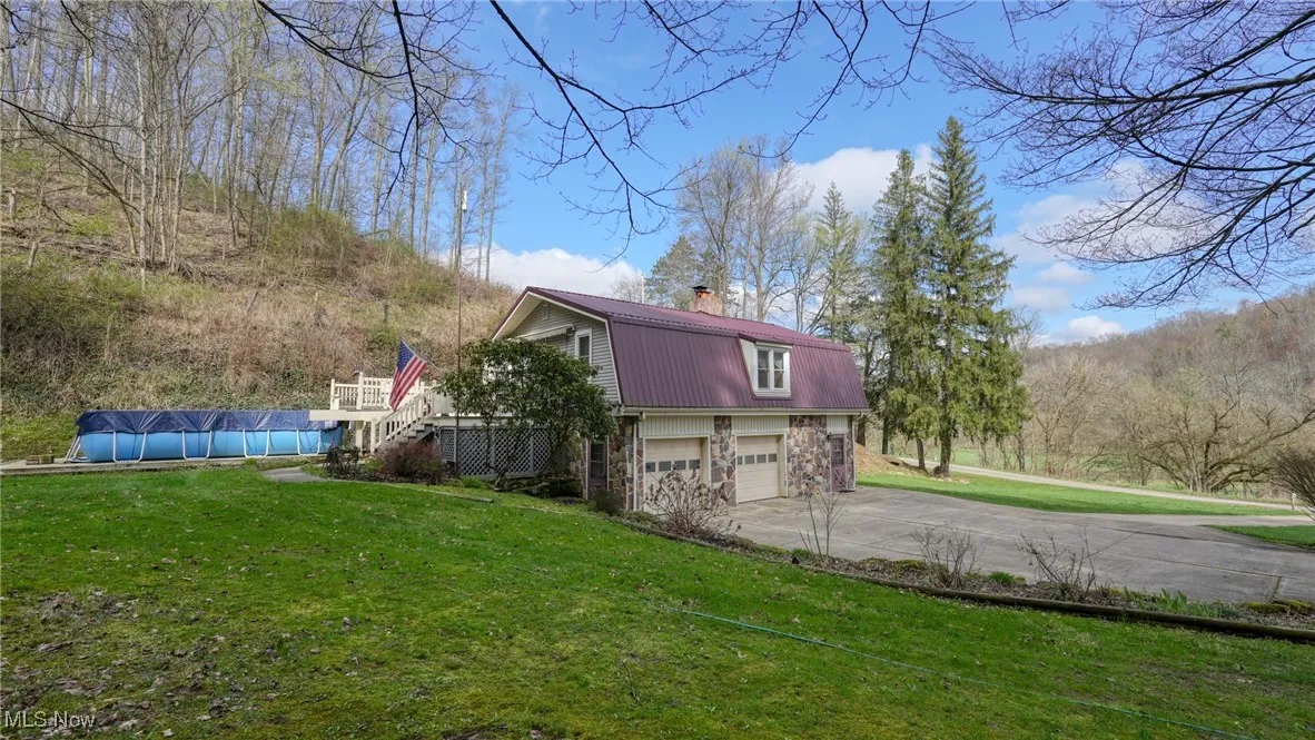 View of property exterior featuring a gambrel roof, metal roof, stairs, a garage, and driveway