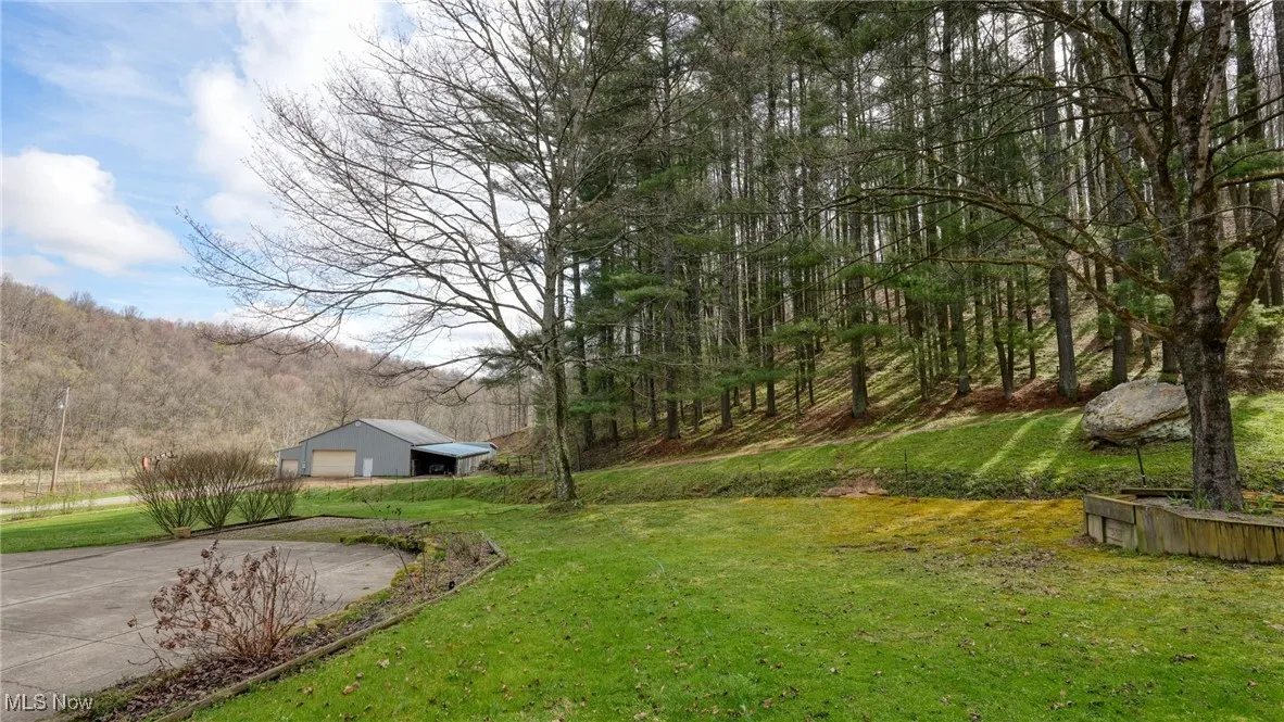 View of yard with a garage, driveway, a view of trees, and an outbuilding