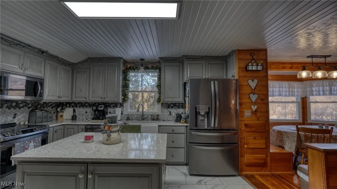 Kitchen with a kitchen island, appliances with stainless steel finishes, gray cabinets, and light stone counters