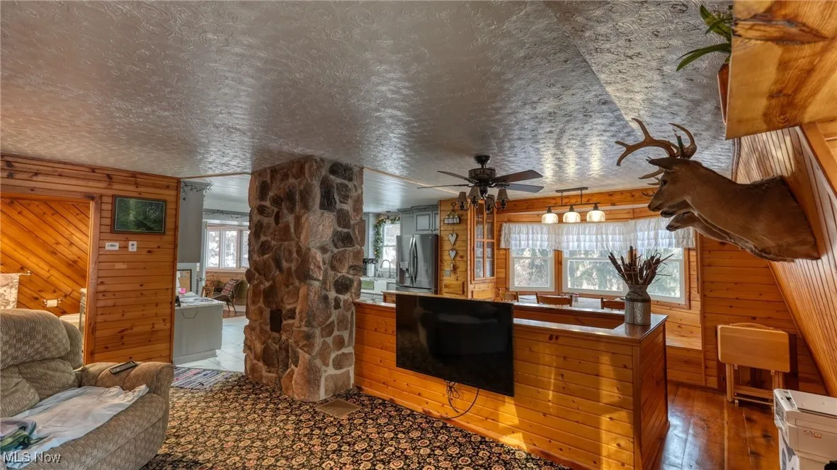 Living room with hardwood / wood-style floors, wooden walls, a textured ceiling, and ceiling fan