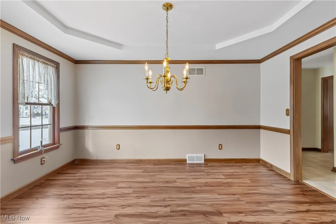 Unfurnished dining area featuring a notable chandelier, light hardwood / wood-style floors, and a raised ceiling