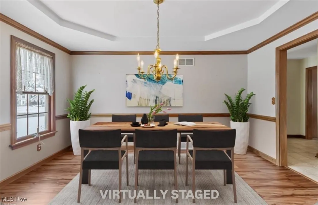 Dining area with a tray ceiling, wood finished floors, visible vents, and a notable chandelier
