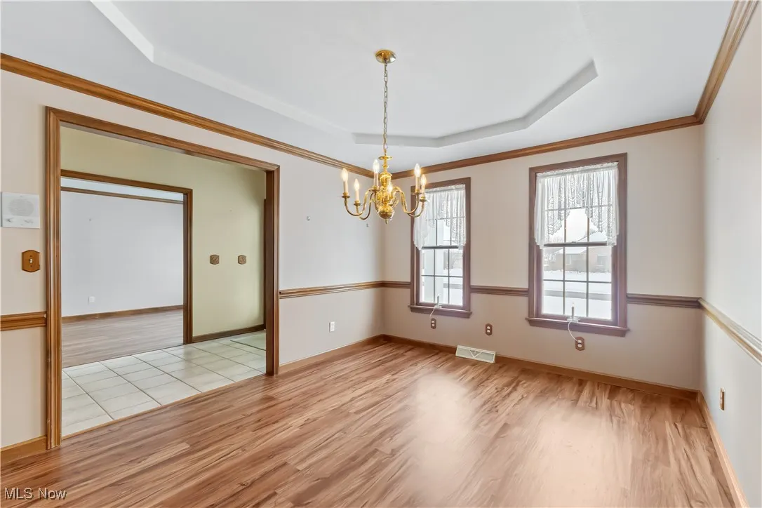 Empty room featuring crown molding, a notable chandelier, light hardwood / wood-style floors, and a tray ceiling