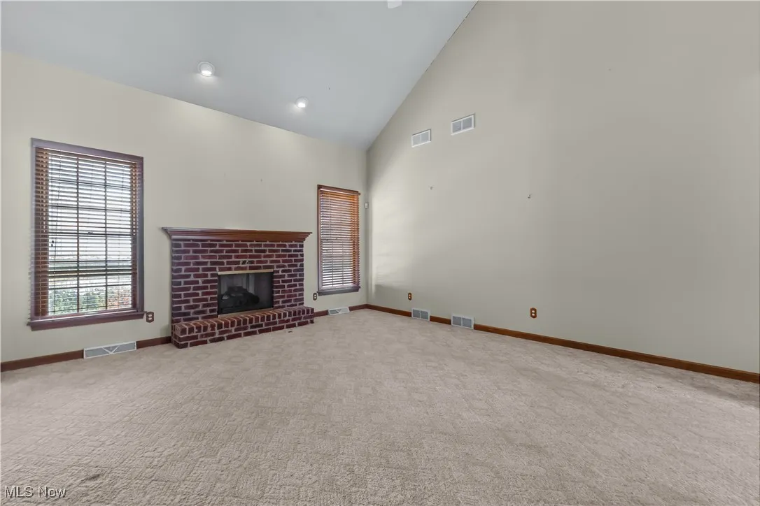 Unfurnished living room featuring carpet flooring, high vaulted ceiling, and a brick fireplace