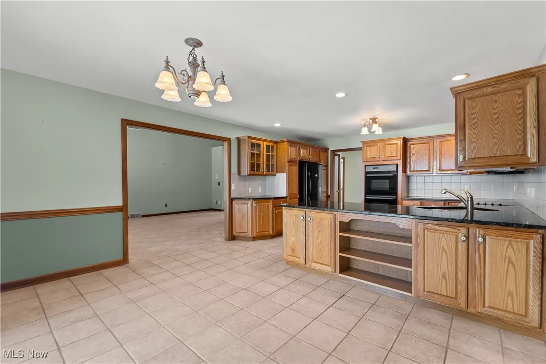 Kitchen with decorative light fixtures, sink, dark stone countertops, backsplash, and black appliances