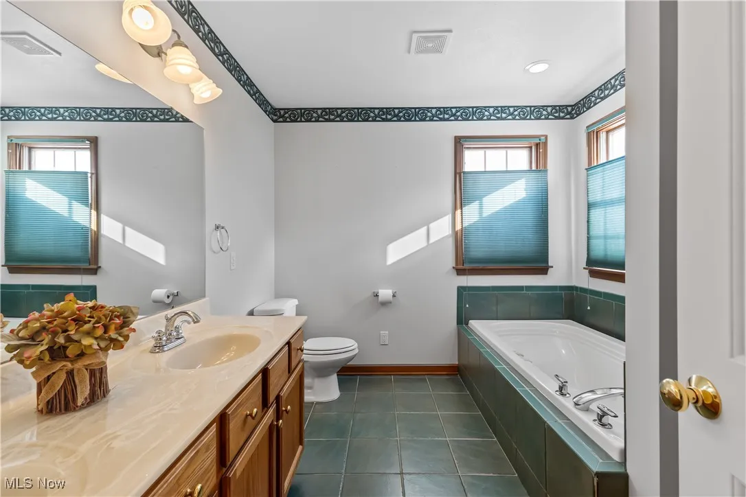 Bathroom featuring vanity, tiled tub, plenty of natural light, and tile patterned floors