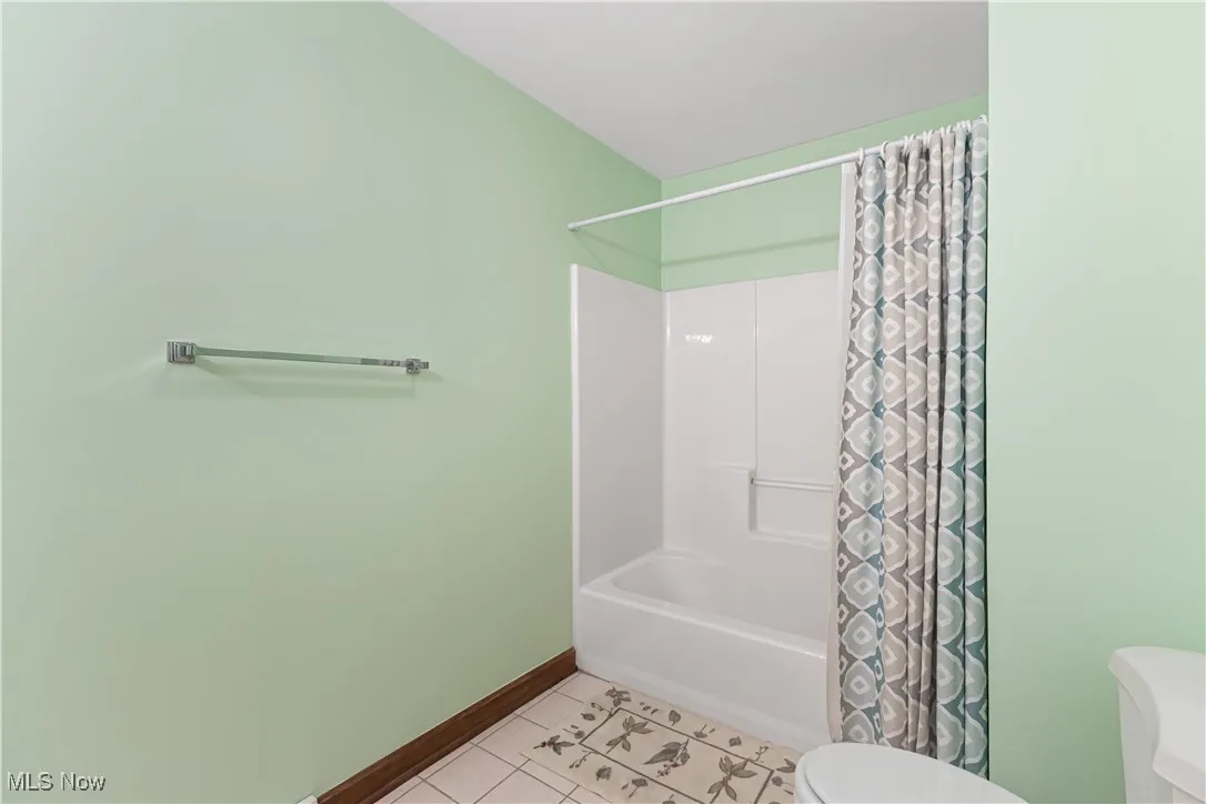 Bathroom with shower / bathtub combination with curtain, tile patterned floors, and toilet