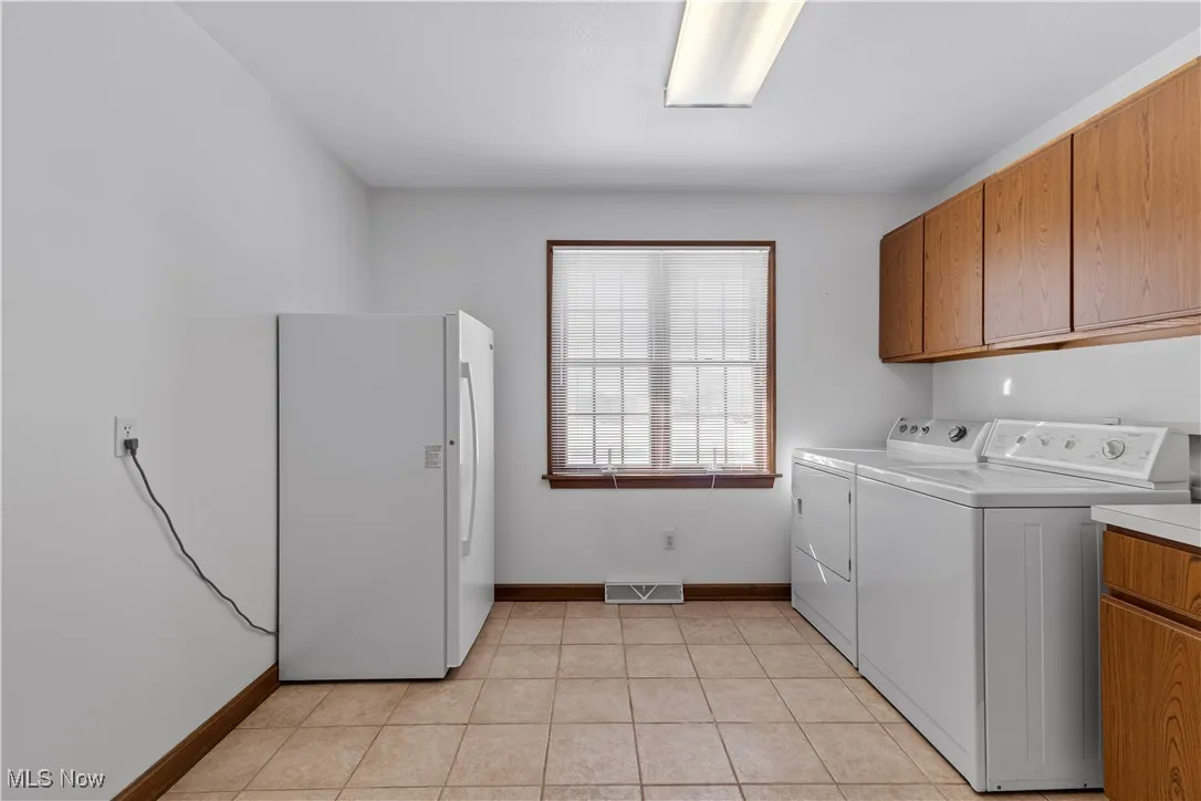 Washroom with light tile patterned flooring, cabinets, and washing machine and dryer