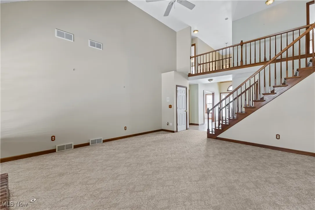 Unfurnished living room with ceiling fan, high vaulted ceiling, and carpet