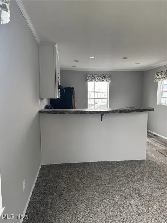 Kitchen with crown molding, fridge, carpet flooring, white cabinets, and kitchen peninsula