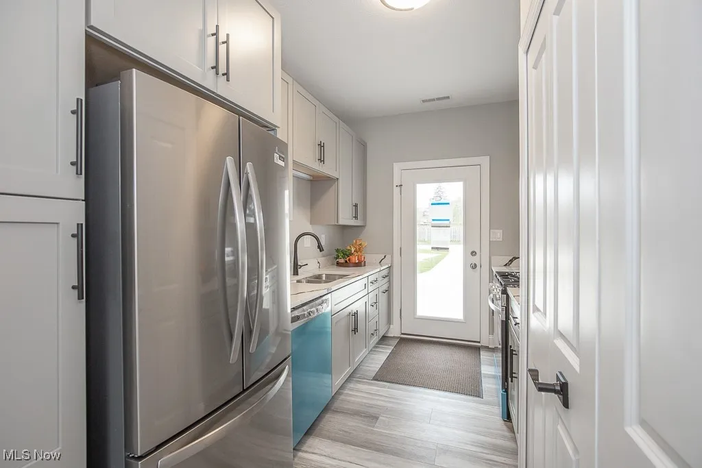 Kitchen with stainless steel appliances, white cabinetry, sink, and light wood-type flooring