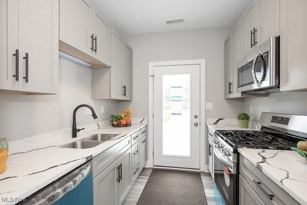 Kitchen featuring a healthy amount of sunlight, sink, stainless steel appliances, and light stone counters