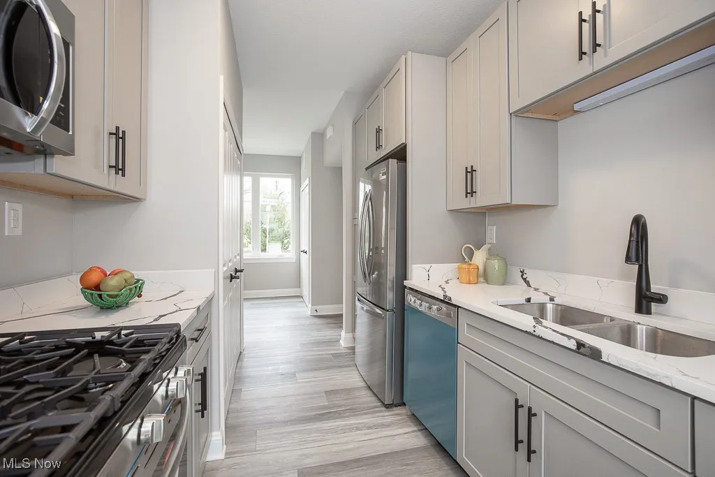 Kitchen with appliances with stainless steel finishes, sink, gray cabinetry, light hardwood / wood-style flooring, and light stone countertops