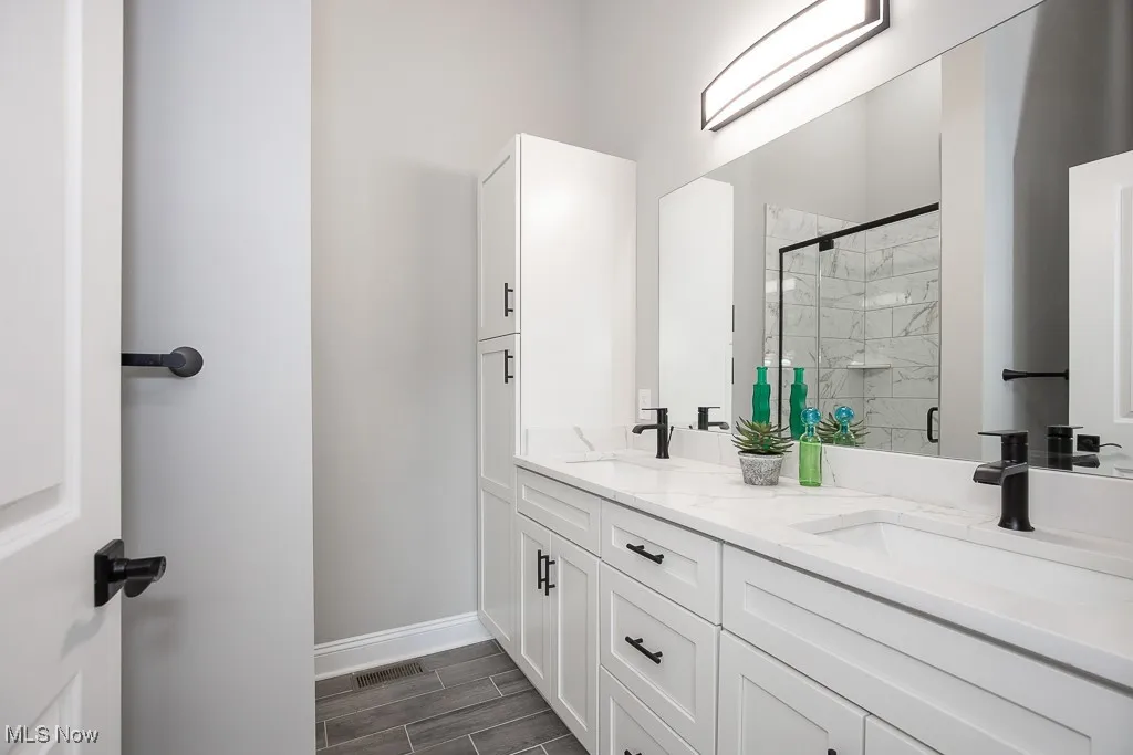 Bathroom with dual sinks, walk in shower, and vanity with extensive cabinet space