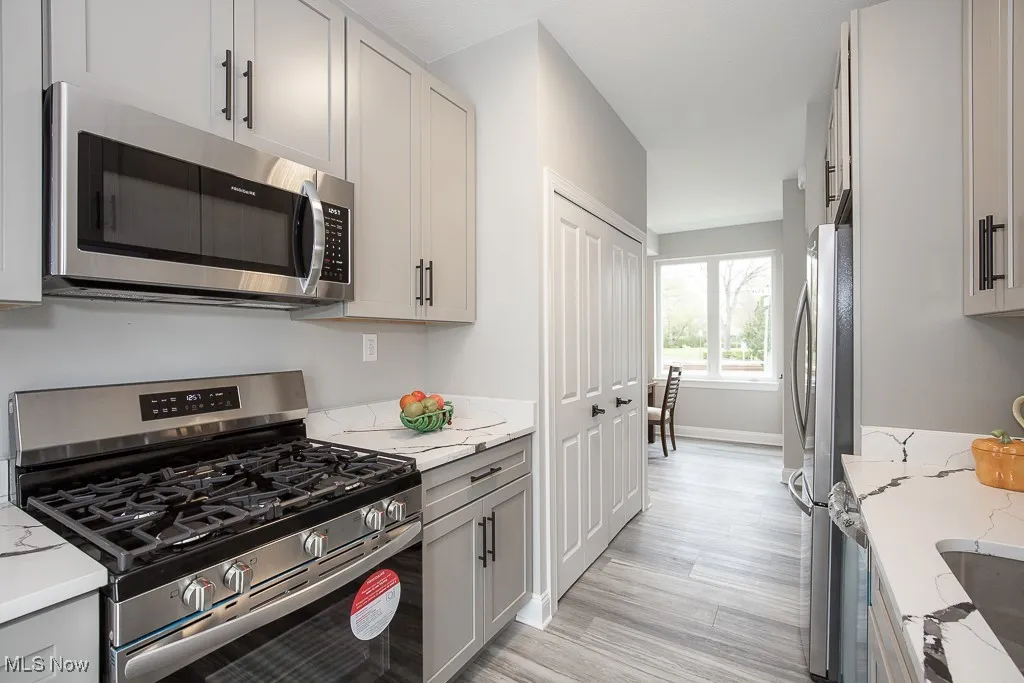 Kitchen with light hardwood / wood-style flooring, stainless steel appliances, and light stone counters