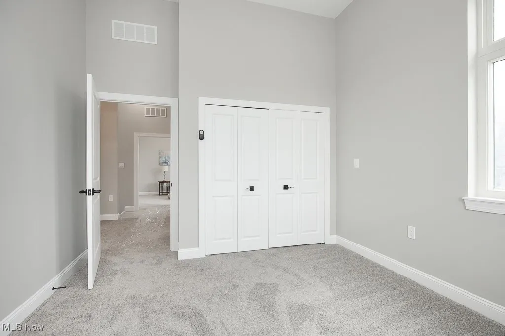 Unfurnished bedroom with light carpet, a closet, multiple windows, and a high ceiling