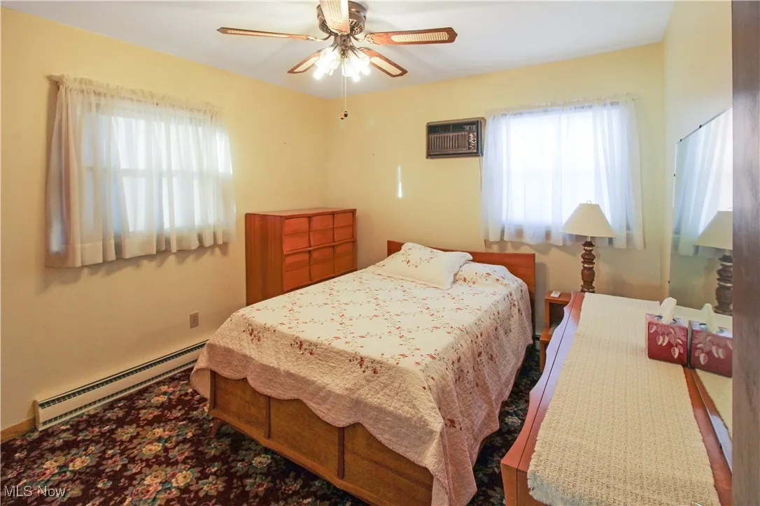 Bedroom with a baseboard radiator, an AC wall unit, and ceiling fan