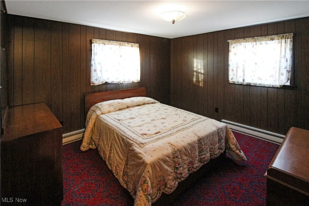 Bedroom featuring wooden walls, multiple windows, and a baseboard heating unit