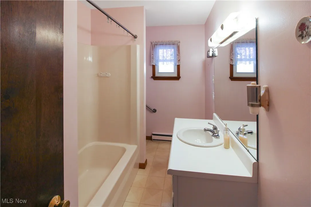 Bathroom featuring a wall mounted AC, shower / tub combination, vanity, tile patterned flooring, and a baseboard heating unit