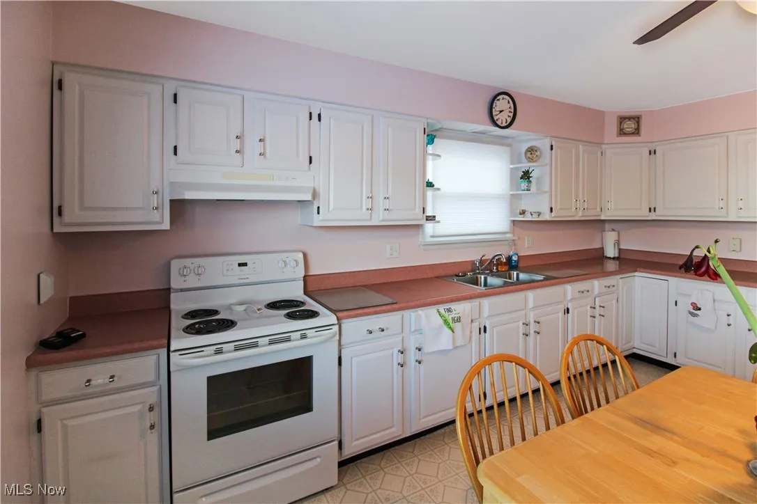 Kitchen with electric stove, white cabinetry, ceiling fan, and sink