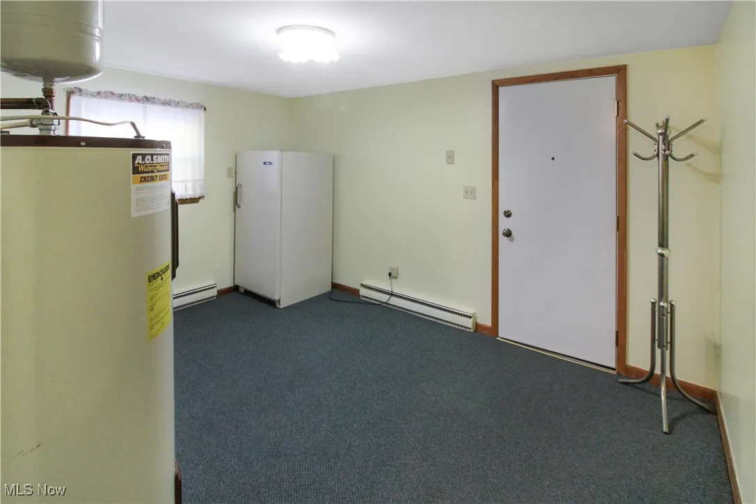 Basement with gas water heater, dark carpet, and baseboard heating