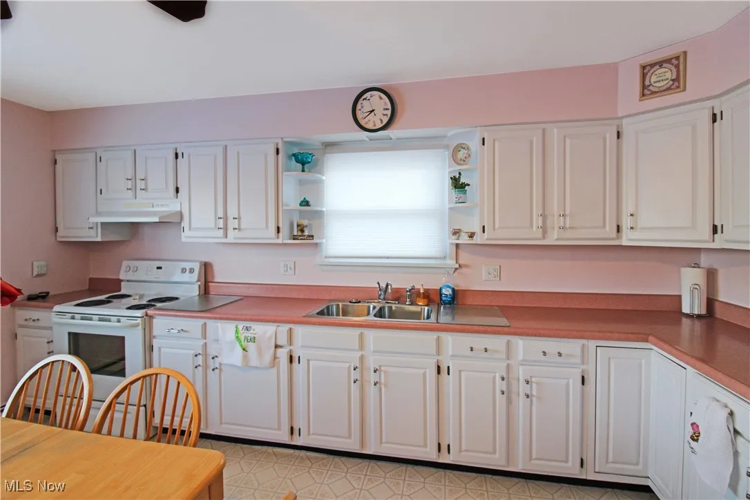 Kitchen featuring sink, white electric range, and white cabinets