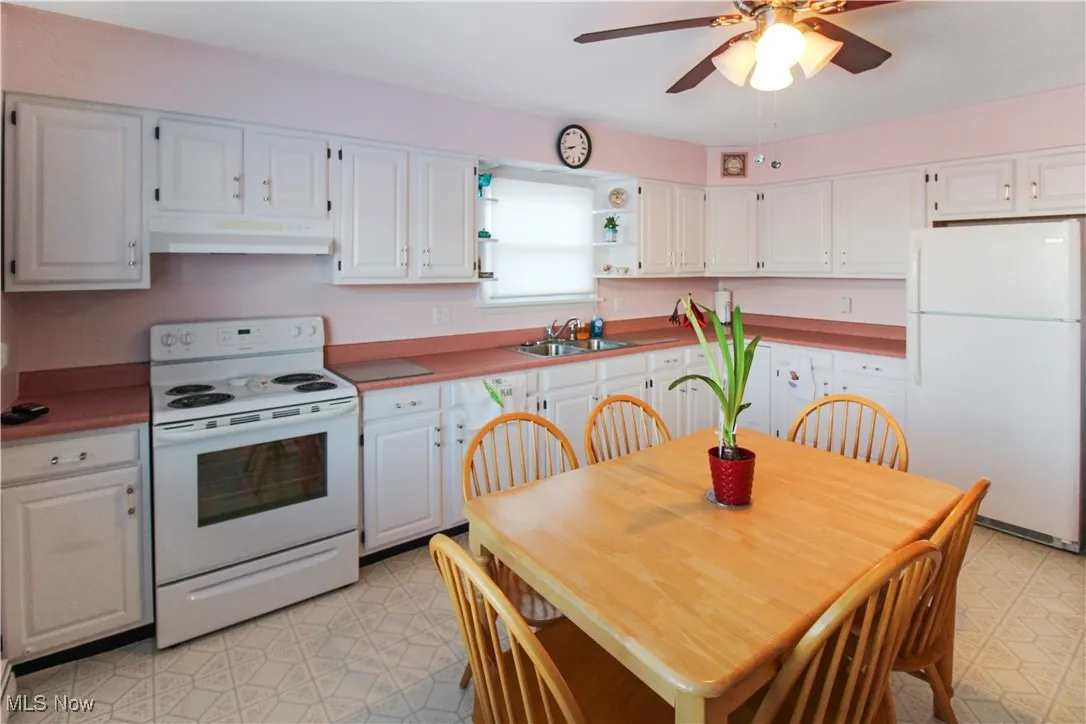 Kitchen with white cabinetry, sink, ceiling fan, and white appliances