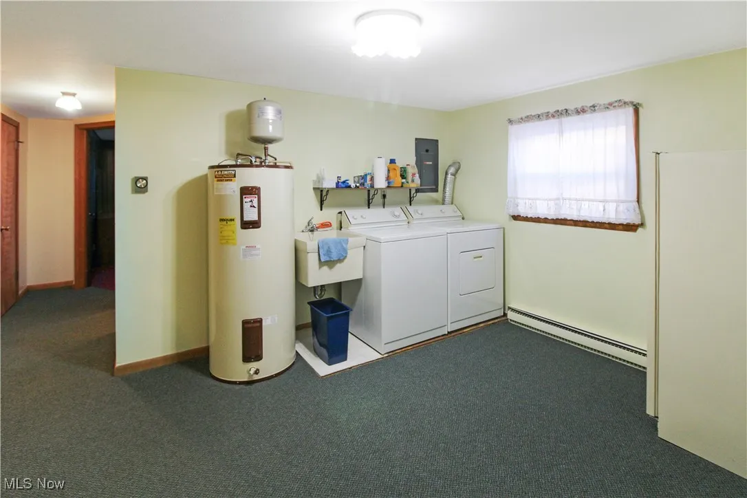 Laundry area featuring washing machine and clothes dryer, sink, baseboard heating, dark carpet, and electric water heater