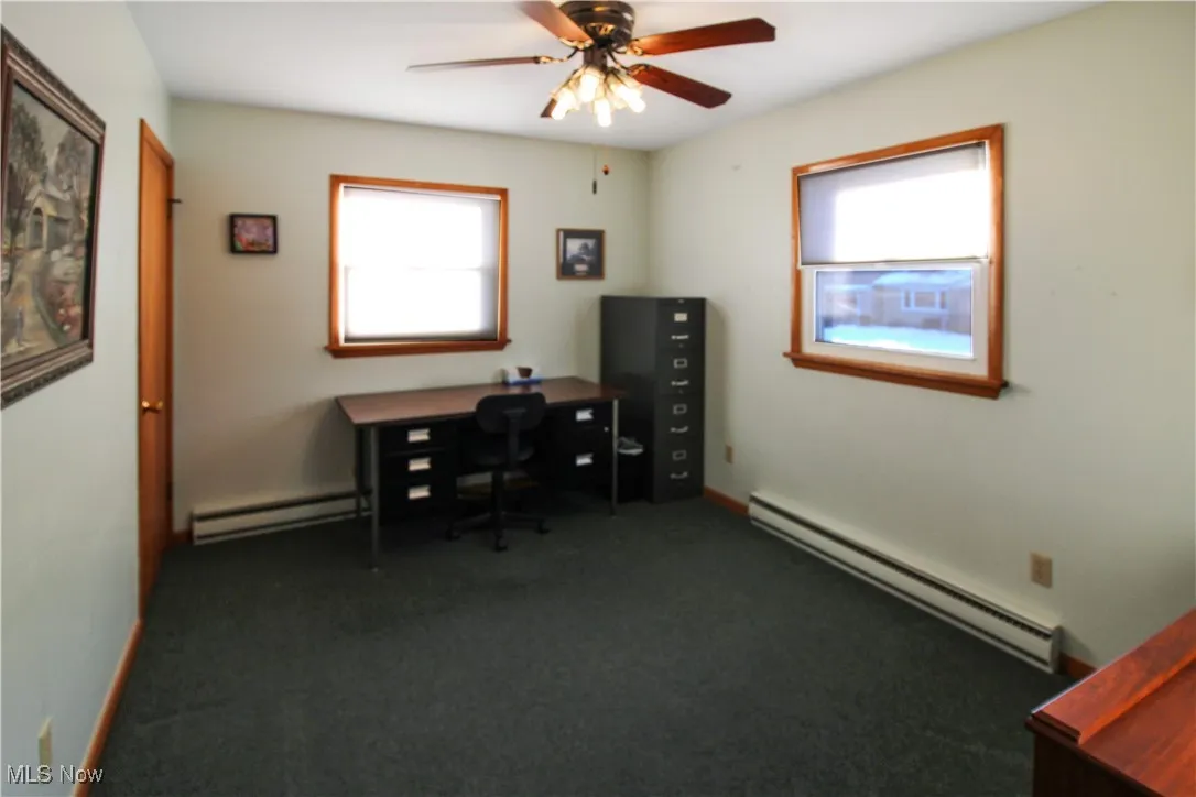 Office space with ceiling fan, a baseboard radiator, and dark carpet