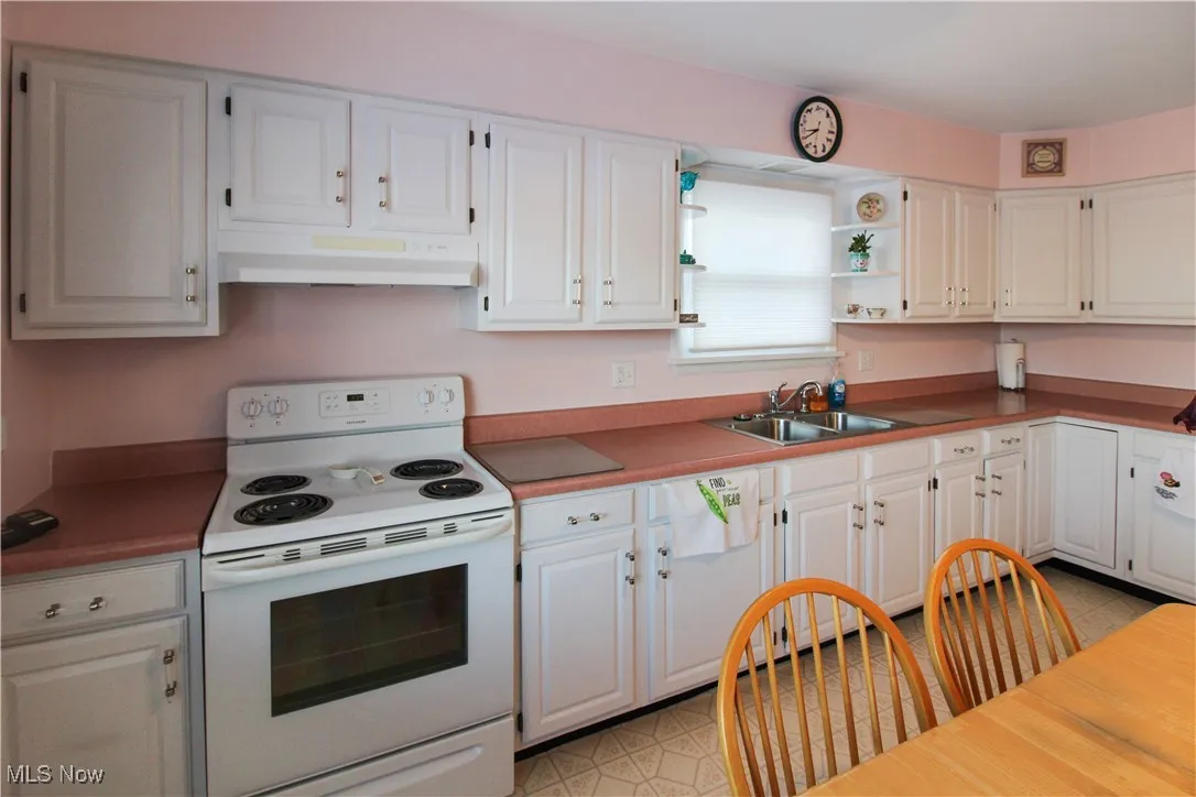 Kitchen featuring white cabinetry, white electric stove, dishwashing machine, and sink