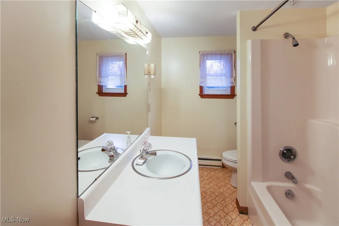 Full bathroom featuring a healthy amount of sunlight, toilet, shower / bathing tub combination, and a baseboard heating unit