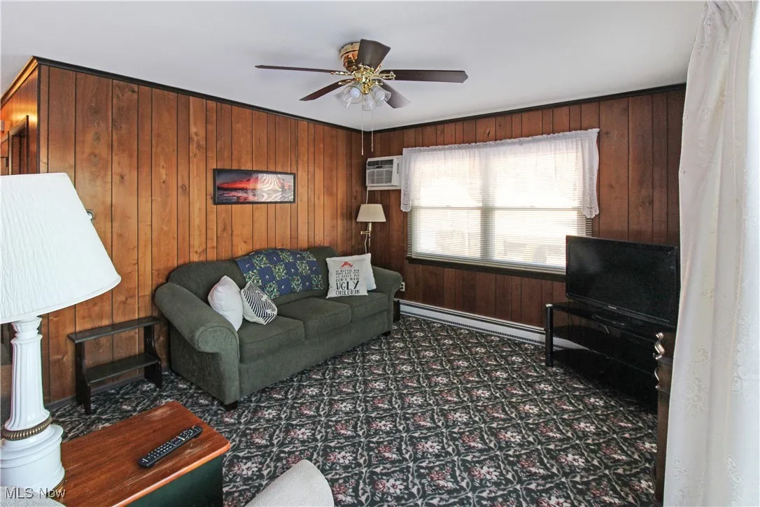 Living room featuring ceiling fan, a baseboard radiator, wooden walls, and a wall mounted AC