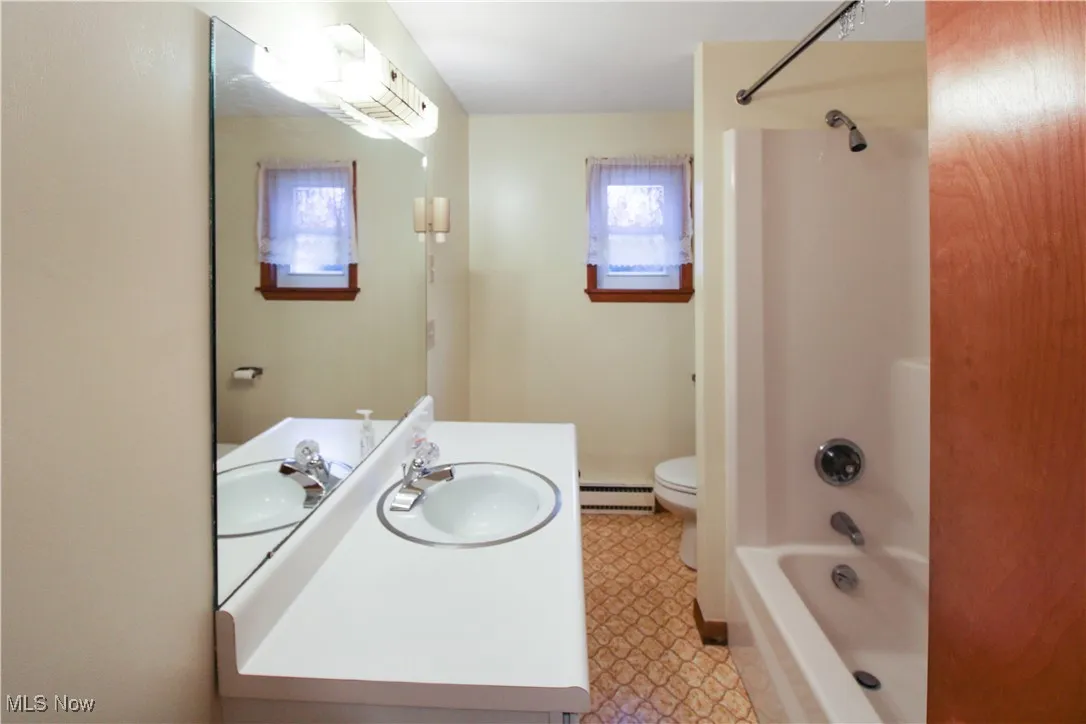 Full bathroom with baseboard heating, washtub / shower combination, vanity, and toilet
