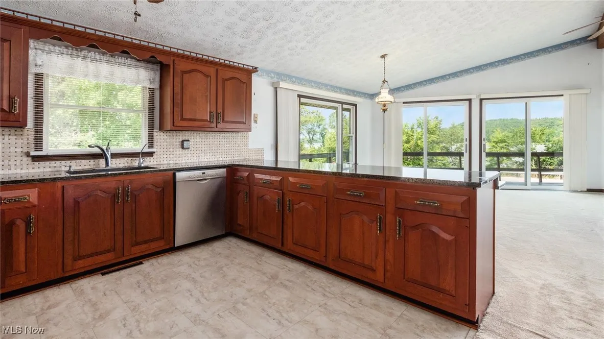 Kitchen with lofted ceiling, sink, decorative light fixtures, stainless steel dishwasher, and kitchen peninsula