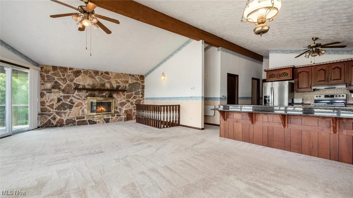 Kitchen with a breakfast bar, vaulted ceiling with beams, light colored carpet, stainless steel appliances, and a fireplace