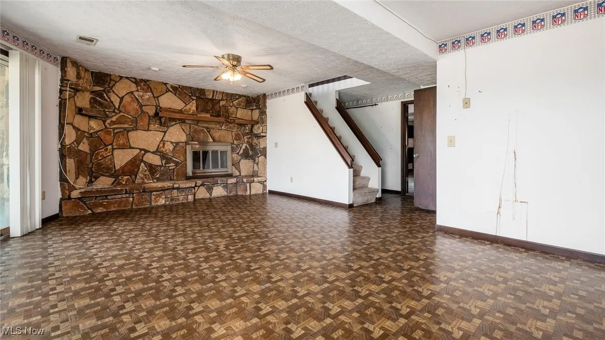 Unfurnished living room featuring ceiling fan, a fireplace, a textured ceiling, and dark parquet floors