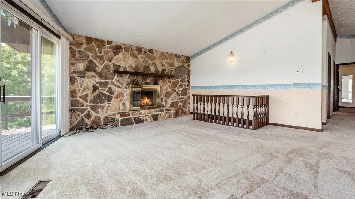 Unfurnished living room featuring light colored carpet, lofted ceiling, a fireplace, and a textured ceiling