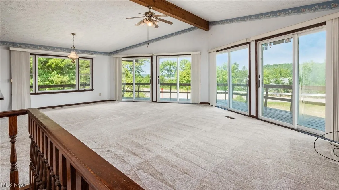 Unfurnished living room featuring lofted ceiling with beams, carpet flooring, a wealth of natural light, and a textured ceiling