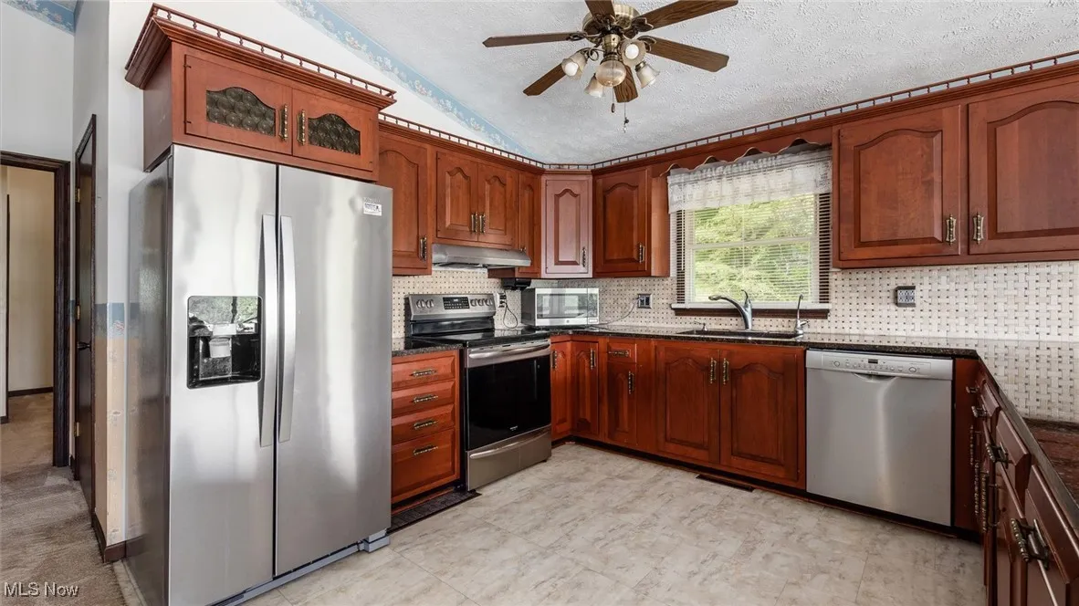 Kitchen with sink, vaulted ceiling, a textured ceiling, appliances with stainless steel finishes, and decorative backsplash