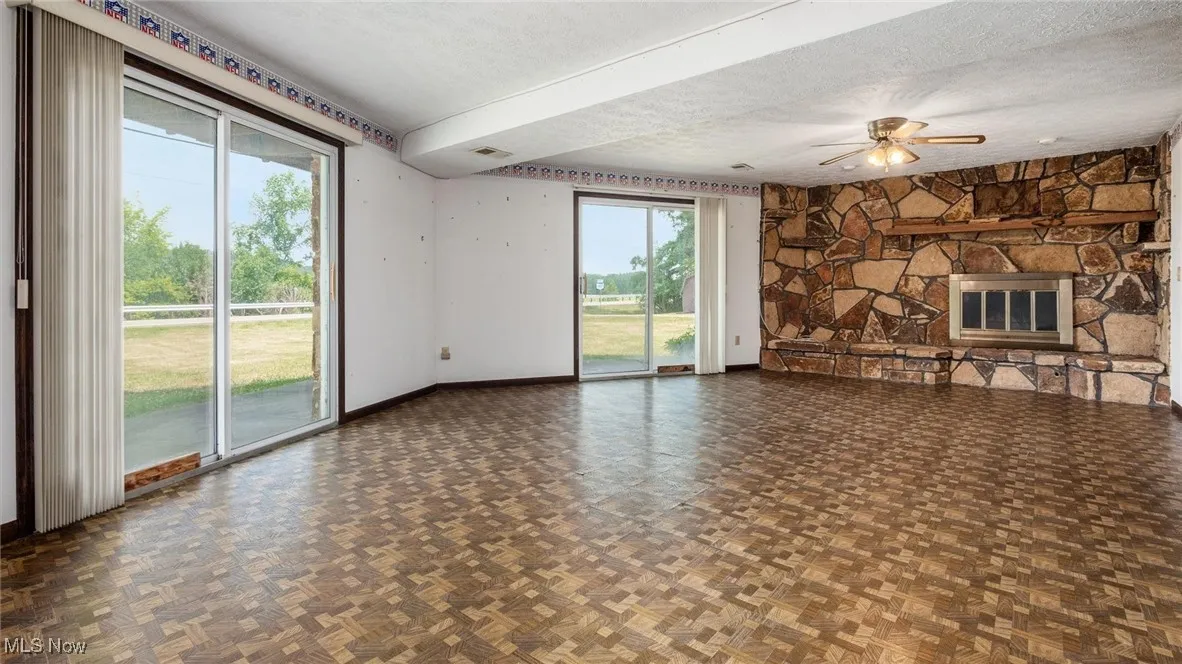 Unfurnished living room with dark parquet flooring, ceiling fan, a fireplace, and a textured ceiling