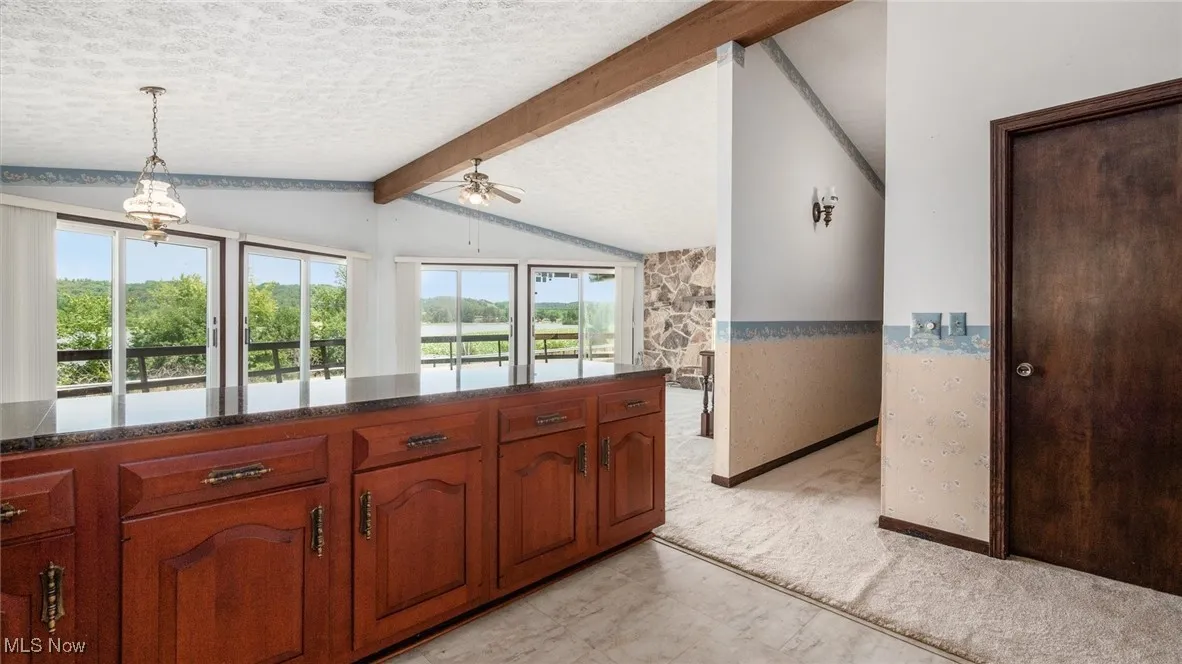 Kitchen with lofted ceiling with beams, light carpet, hanging light fixtures, a textured ceiling, and ceiling fan